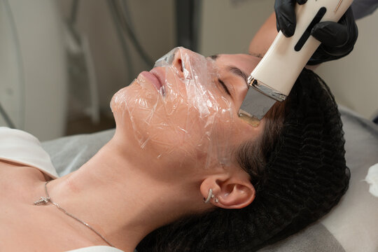 Close up of cosmetologist performing ultrasonic facial peeling on young woman in beauty clinic. Professional skin care treatment using ultrasonic device for deep cleansing and exfoliation. Cosmetology