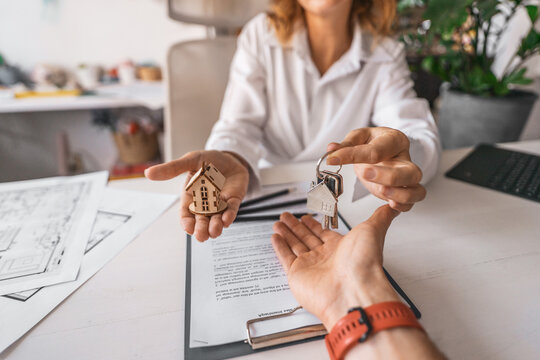 Female realtor signed contract for apartment sale rental and hands keys client over documents with blueprint and house model on table. Concept of mortgage deal, property transfer and secure investment