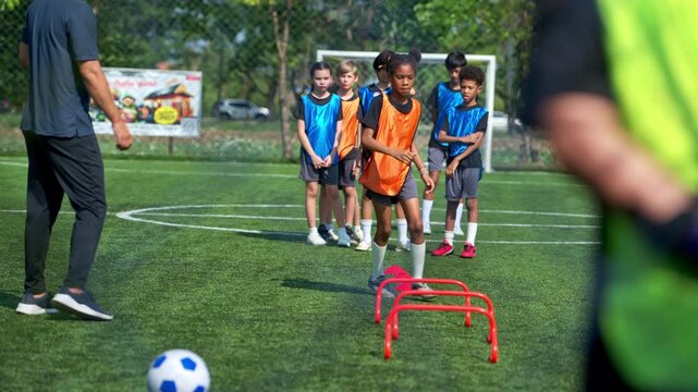 International school girl performing agility drill with hurdles while teammates wait in line behind on soccer field