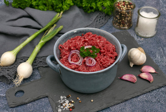 Frisches rohes Rinderhackfleisch in Sch&uuml;ssel mit Fr&uuml;hlingszwiebeln, Knoblauch und Gew&uuml;rzen auf einer Schieferplatte.