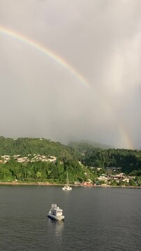 Vertical phone footage of a complete rainbow over a tropical island as seen from a boat at anchor