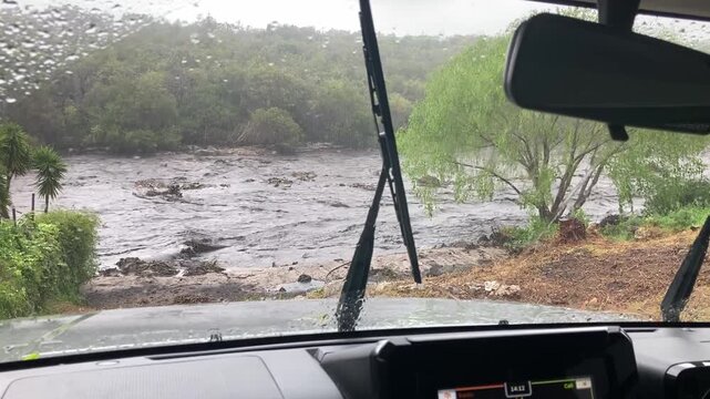 A view through a car windscreen in the rain over a river in full flood