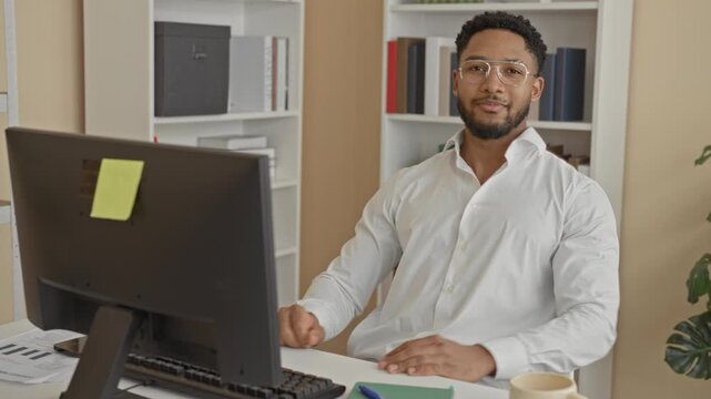 Man at computer forms heart with hands while smiling at camera in office wearing white shirt and glasses; warmth.