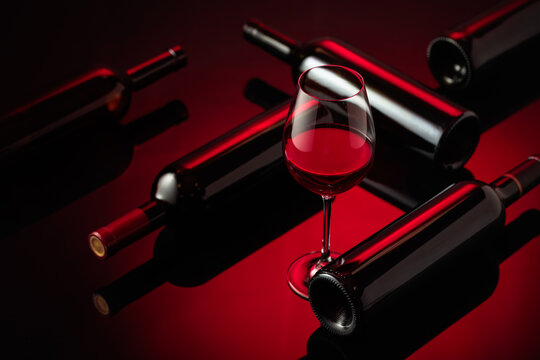 Glass and bottles of red wine on a black reflective background.