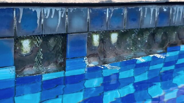 Close-up view of damaged swimming pool tiles with missing pieces and visible structural deterioration. Concept of poor maintenance, repair needs, and aging infrastructure.
