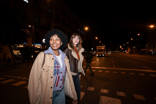 Happy friends smiling and crossing the city street at night