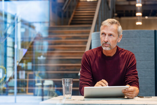 Businessman sitting thoughtfully with tablet in modern office