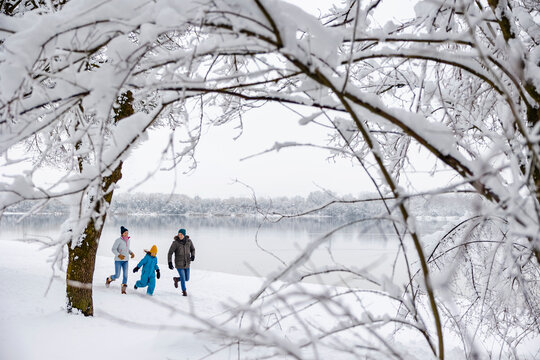 Family running in snow by a lake during winter