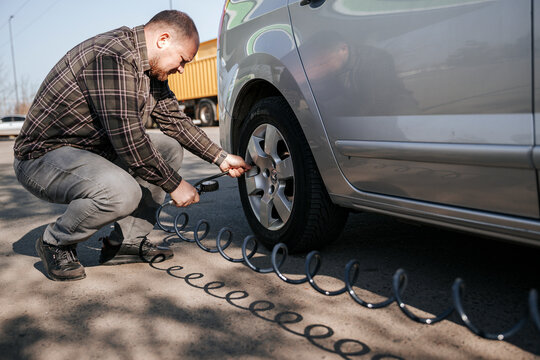 Driver kneeling outdoors checking car tire pressure with air pump