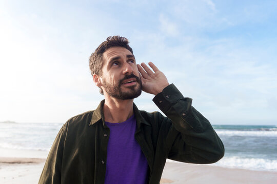 Man listening under sky at beach on sunny day