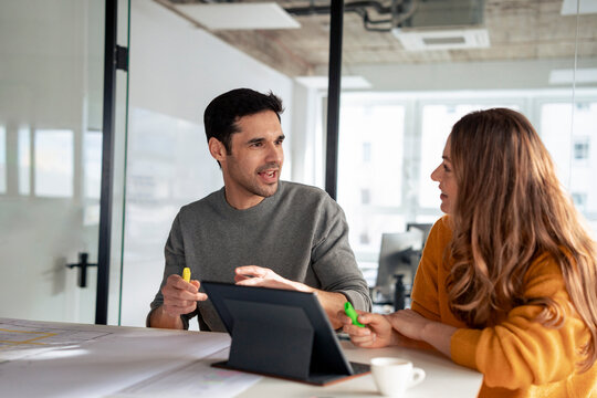 Happy mature architects discussing with tablet PC and blueprints at desk