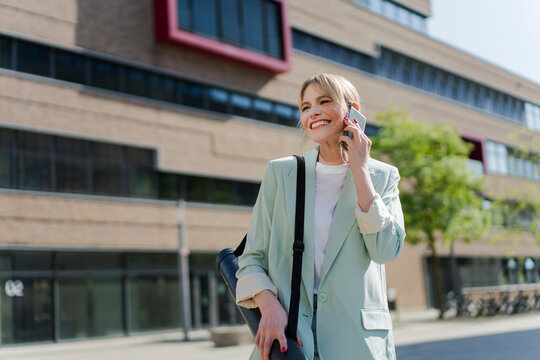 Smiling architect with tube talking on smart phone standing in front of building