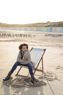 Woman with arms crossed sitting on deck chair at beach