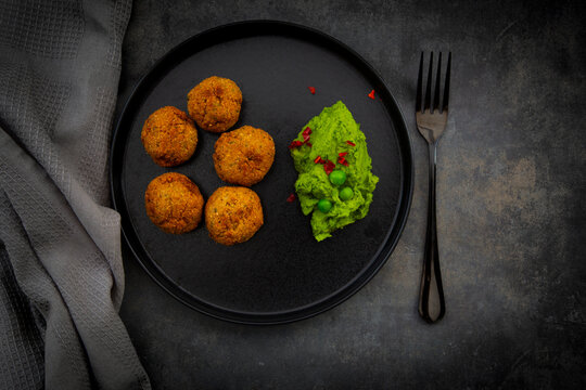 Falafel and pea hummus with chili on a black plate directly above