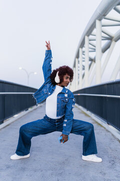 Dancer in denim posing with smartphone on urban bridge