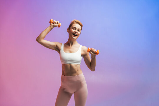 Happy woman exercising with dumbbells against two tone colored background