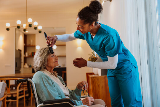 Caregiver combing hair of elderly woman seated in wheelchair indoors