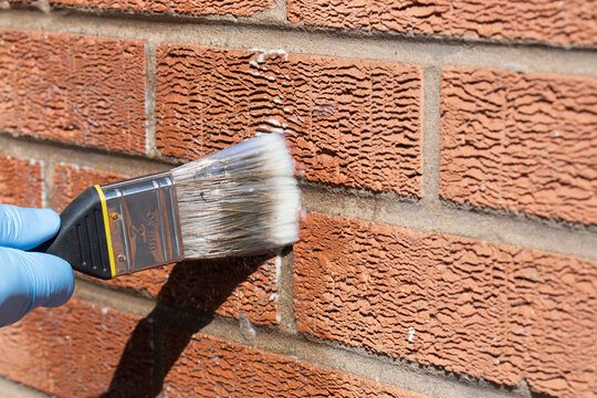 Person sealing an exterior brick wall with a clear waterproof sealant, using a paint brush. Do it yourself home improvement concept.
