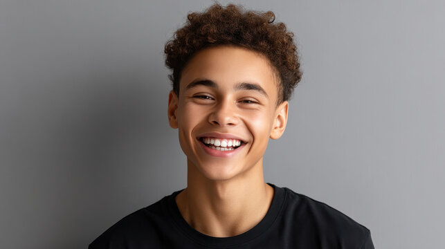 Black teenager portrait smiling young man, curly hair, casual black shirt, studio gray background, bright confident expression, friendly mood, ethnic tolerance concept