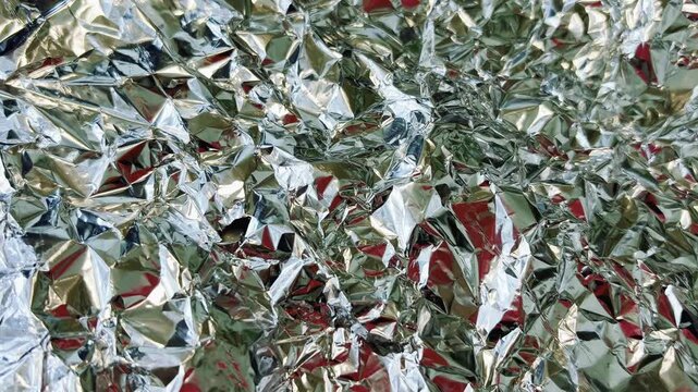 Crumpled silver foil texture with glossy metallic surface. Shiny aluminum background with elegant light reflections and chrome-like foil finish for modern design projects.
