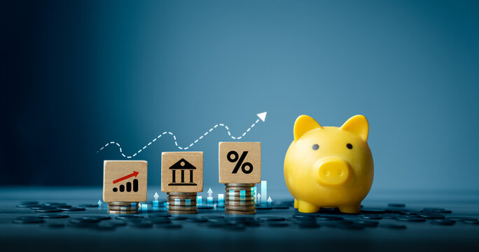 Stacked coins with wooden blocks showing growth chart, bank icon, and percentage symbol beside yellow piggy bank, representing financial planning, savings, interest rate, and investment growth concept