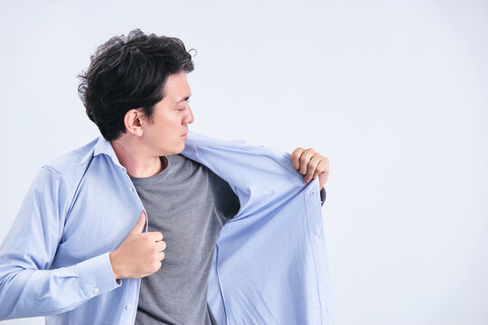 白背景の前で身だしなみや汗の匂いを気にしてワイシャツを着替える30代の男性
