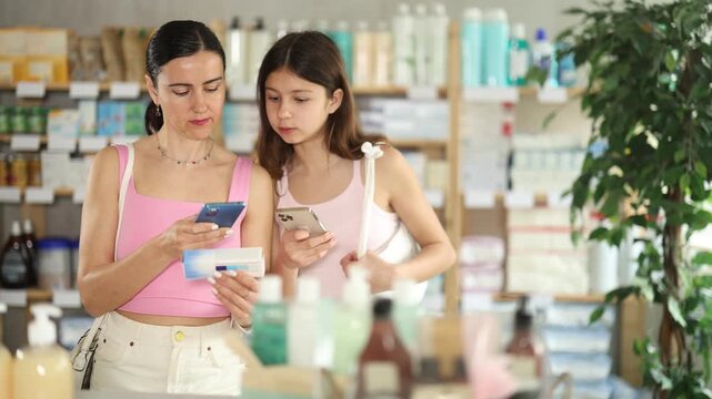 Attentive middle-aged woman with daughter scanning QR box of ointment held in hand in chemistry. High quality 4k footage