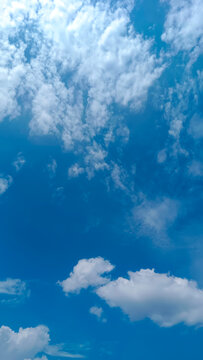 White cumulus clouds drift across a vivid blue sky in vertical composition with expansive copy space, suited for nature-themed design, wellness visuals, and mobile backgrounds.