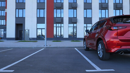Obraz premium Single Red SUV On An Empty Parking Lot In Front Of Modern Business Building 