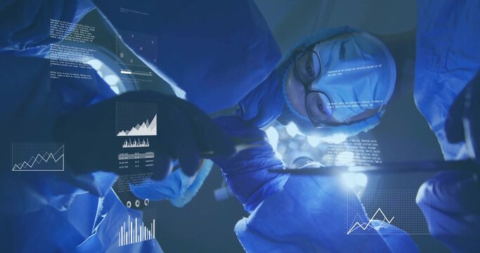 Operating surgical team in blue gowns, masks leaning over patient at OR table, headlamp and HUD