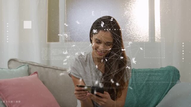 Woman on couch picking card and tapping smartphone, animating currency overlay for making payment