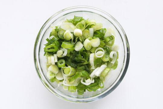 Top view of a clear glass bowl of sliced or chopped green spring onions, isolated on a clean white background.