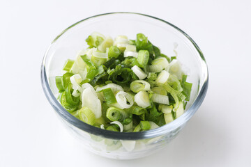 Obraz premium A clear glass bowl of sliced or chopped green spring onions, isolated on a clean white background.