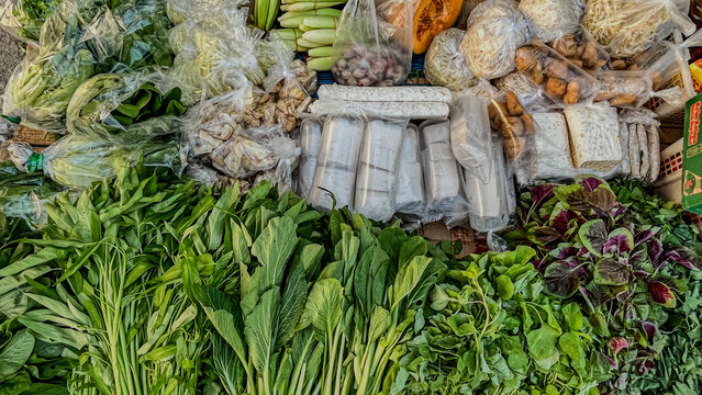 Fresh tempeh and tofu surrounded by various green vegetables at a traditional market in Samarinda, East Kalimantan.