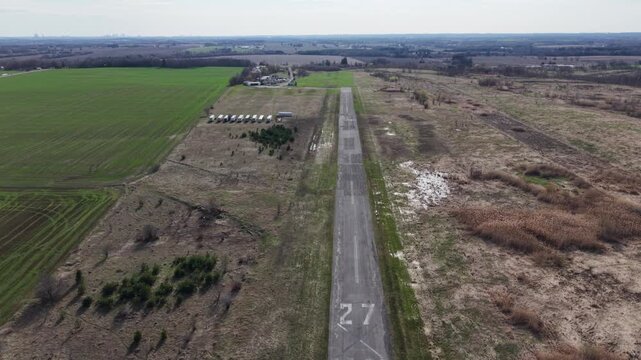 Forward-moving drone shot over the cracked asphalt of a decommissioned runway, featuring faded number 27 markings and surrounding rural landscapes
