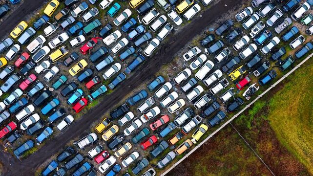 Diagonal aerial view of large automotive recycling yard. Slanted high angle drone photo of numerous colored cars parked in rows at an industrial scrap facility.