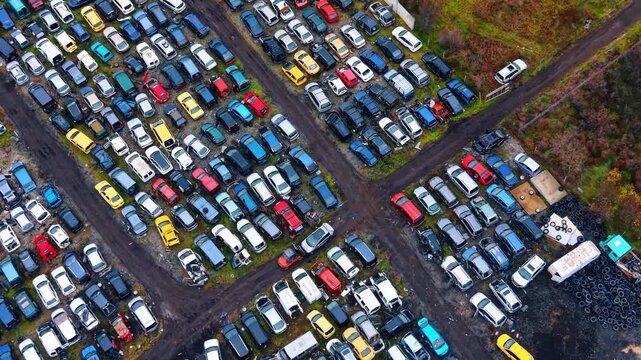 Aerial perspective of car cemetery with various colored vehicles. High angle view of a large auto salvage yard with numerous cars organized by paths and a tire pile.