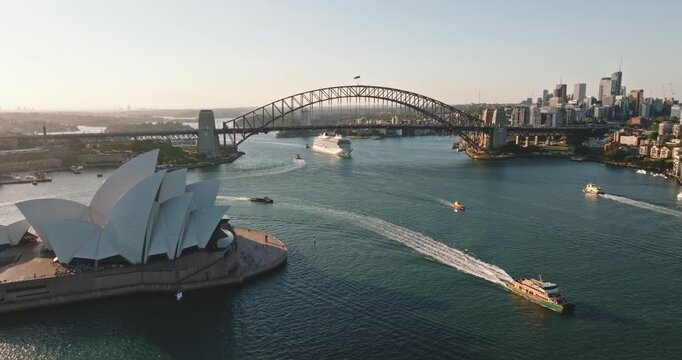 Sydney cityscape featuring Opera House and iconic Harbor Bridge spanning the busy harbor with cruise ship and ferries navigating the water during a warm summer day, illustrating travel and tourism