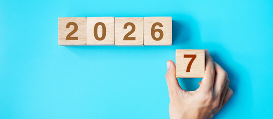 Naklejka premium hand holding wooden cube block with 2027 text on blue background. Resolution, plan, review, goal, start and New Year holiday concepts