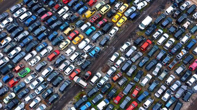 Forklift loader moving a car in salvage yard. Aerial view of an orange loader moving a scrap vehicle between rows at an auto recycling center.