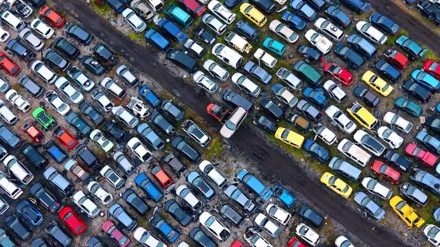 Drone perspective of automotive salvage yard and recycling facility. High angle view of various colored old cars parked in rows at an industrial scrap yard under daylight.