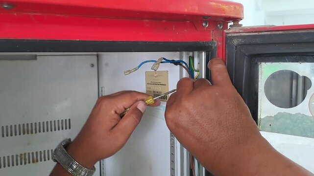 PAMEKASAN, INDONESIA - DECEMBER 18, 2025: Handheld footage of an Asian electrician repairing the power wiring of a commercial showcase cooler. Technician troubleshooting electrical connections mainten