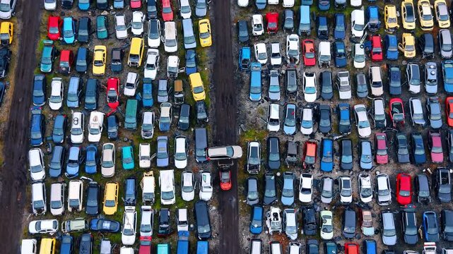 Loader equipment carrying scrap car in junkyard. Top down view of industrial equipment transporting a car within an organized auto recycling facility lot.