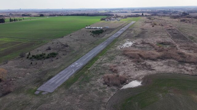 High-angle aerial orbit shot of the cracked asphalt of runway 27 at the abandoned Toronto Markham Airport, surrounded by overgrown rural fields