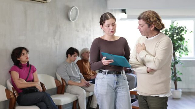 Serious female secretary talking with middle-aged man concerning documents while standing in reception area. High quality 4k footage