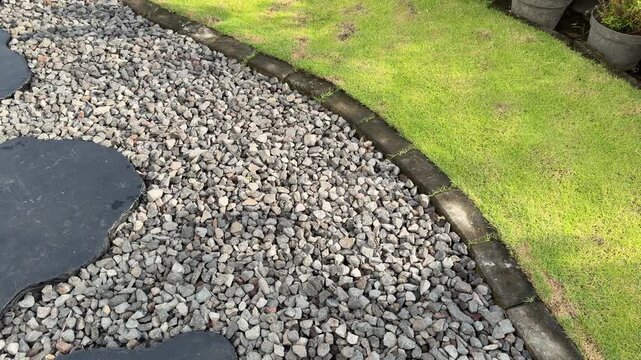 Curved gravel path borders lush green lawn. Dark slate stepping stones add elegant contrast. Natural stone edging defines garden boundary clearly. Sunlight enhances texture of stones and grass