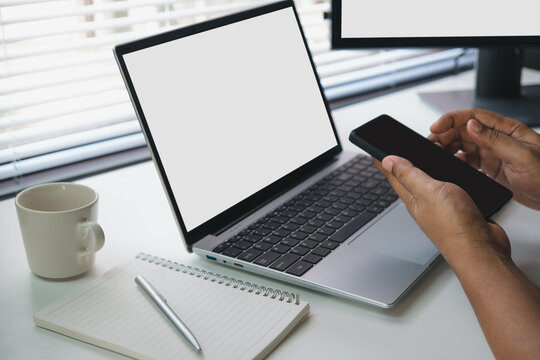 Remote work using smartphone next to laptop in modern workspace, checking messages and managing tasks on mobile device, productivity and digital communication concept