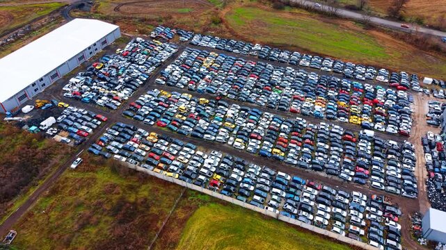 Industrial car recycling site with warehouse and vehicle rows. Aerial perspective of a professional car dismantling facility with organized rows of scrap metal vehicles.