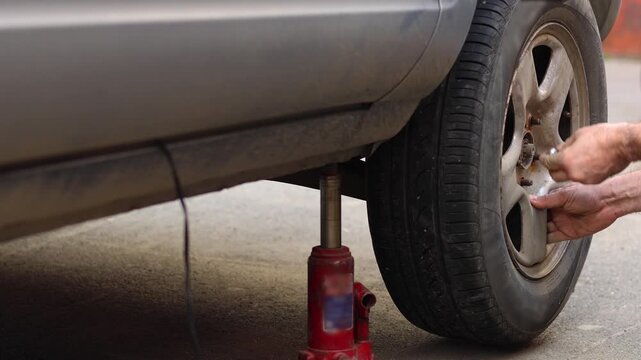 A man installs a repaired wheel and begins tightening the lug nuts. Close-up of his hands. The car is being lifted with a hydraulic jack. 4k footage.