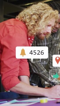 Vertical video: Two men sketching at studio, phone sparking floating social metrics shaping design